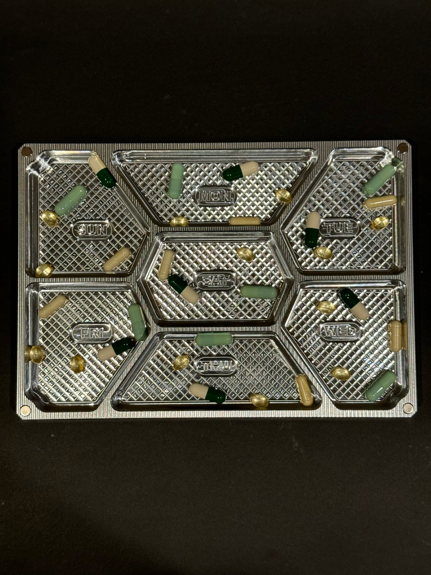 Top view of raw machined Vitamin Vault Mega filled with tablets and capsules across seven labeled daily compartments.