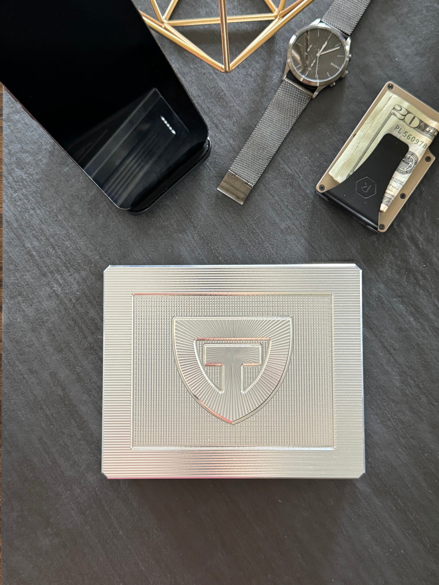 Closed TRT Vault Mini in Raw Machined on a dark desk with a phone, watch and cardholder.