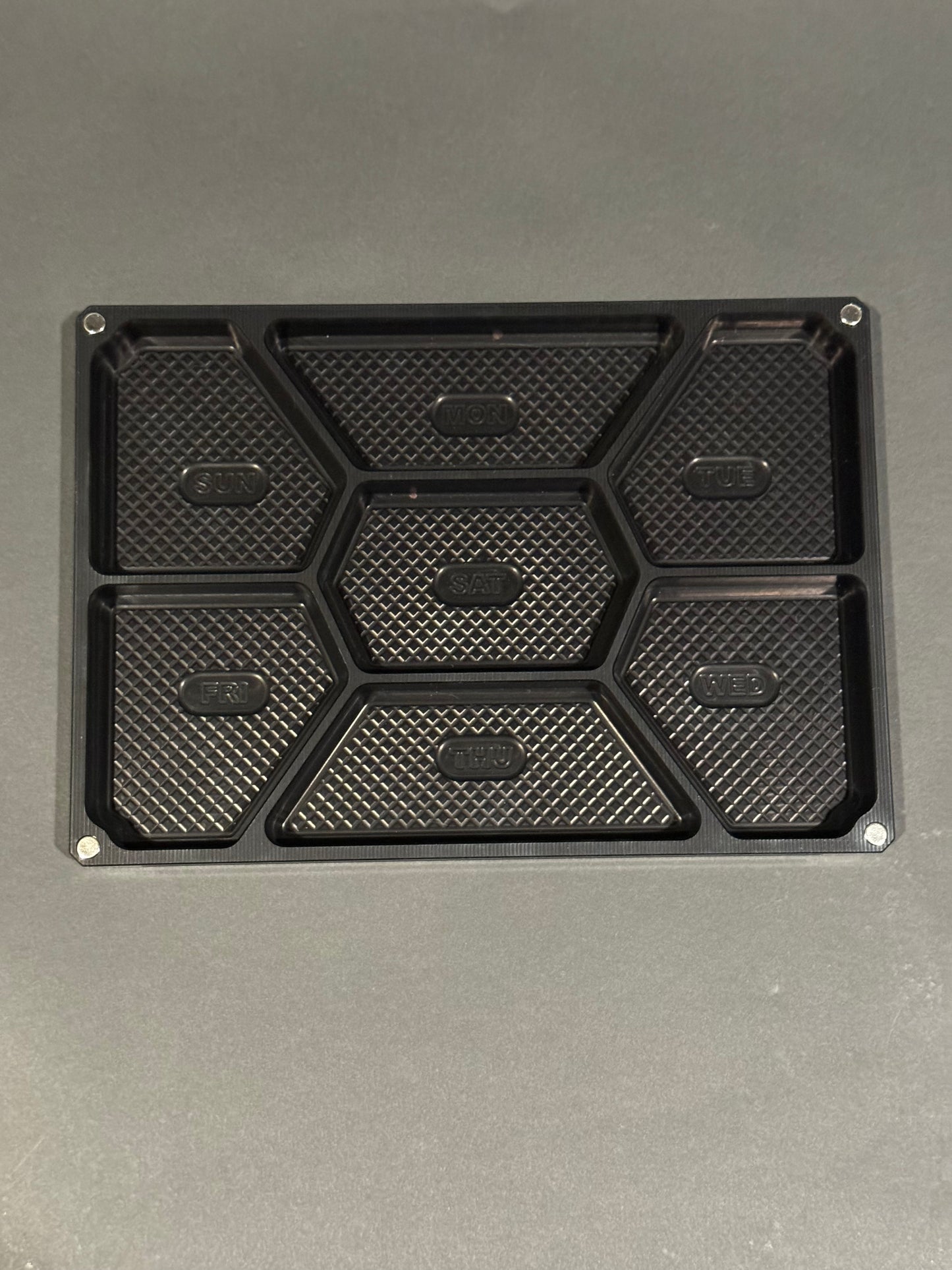 Top view of empty anodized black Vitamin Vault Mega with seven labeled daily compartments.