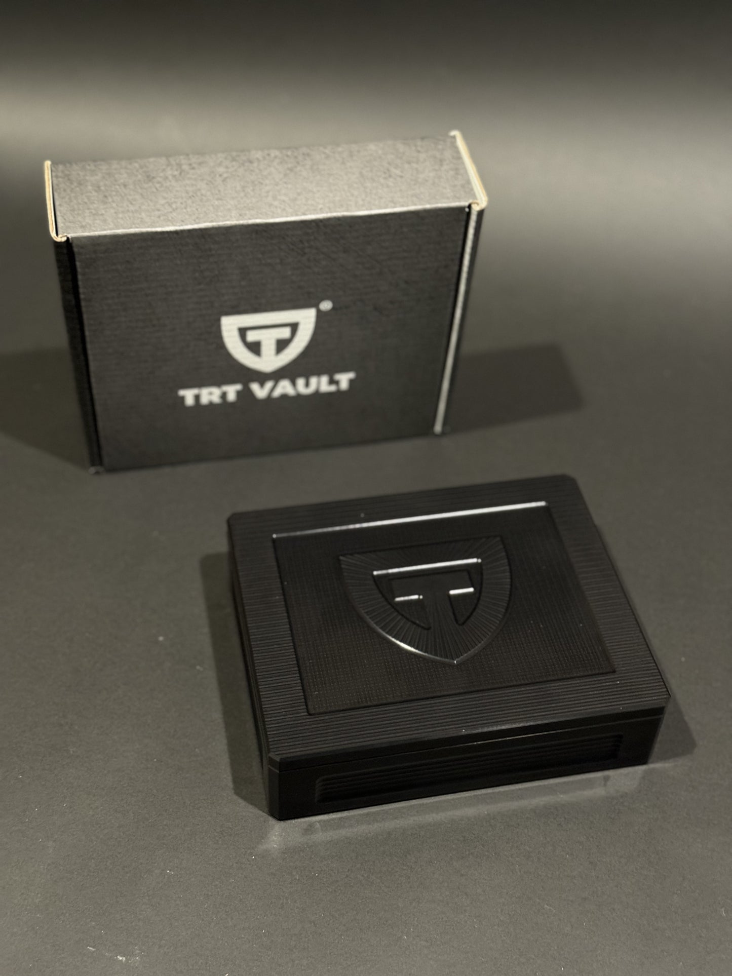 Closed TRT Vault Mini in Anodized Black beside its branded packaging.