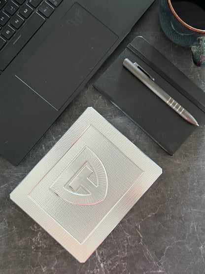 Closed TRT Vault Mini in Raw Machined on a desk with a laptop, notebook and pen.