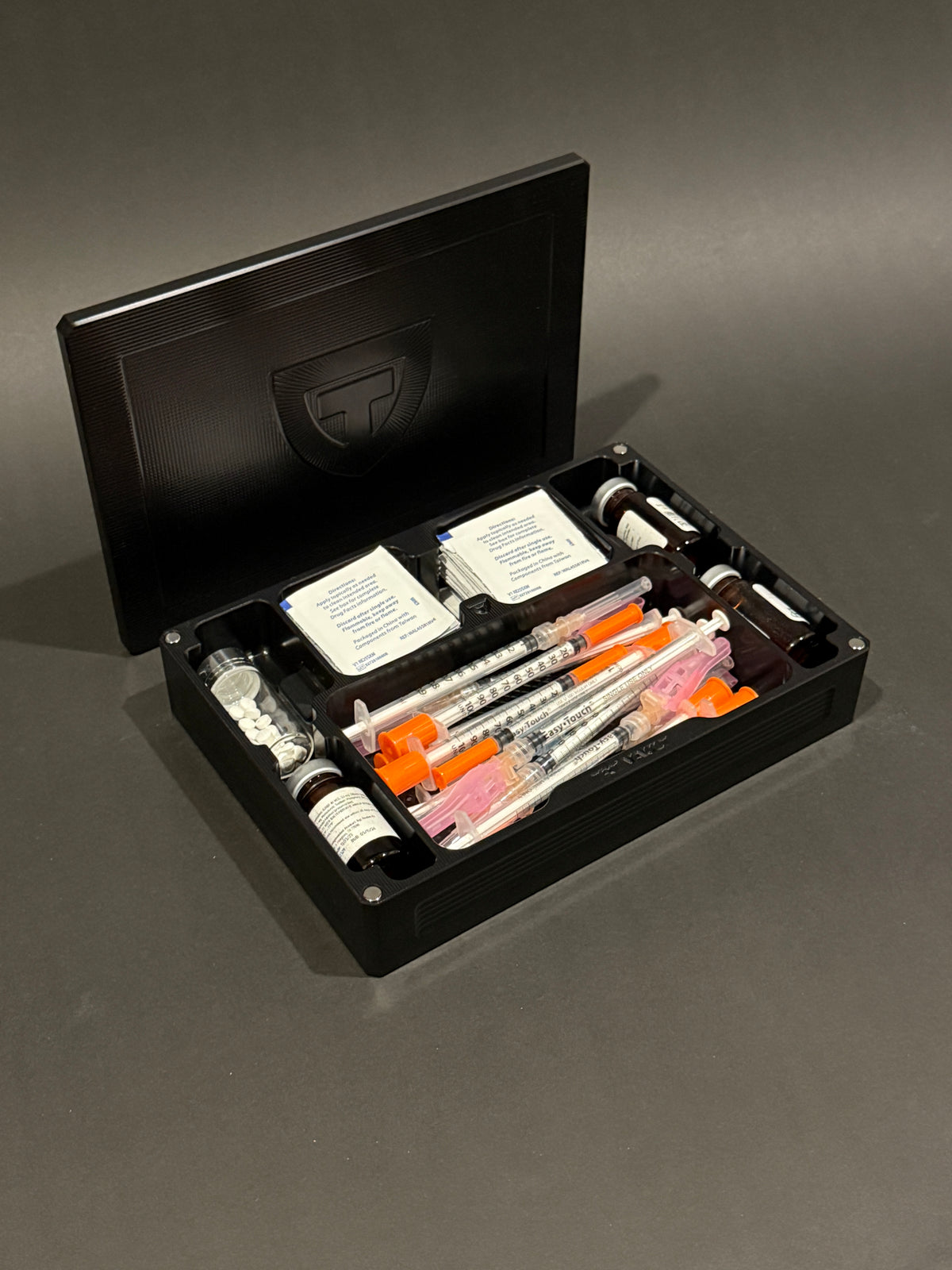 TRT Vault Mega in Anodized Black holding vials, syringes and alcohol swabs.