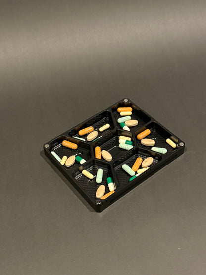 Anodized black Vitamin Vault Mini Lidless shown filled with assorted vitamins and supplements in seven individual compartments.