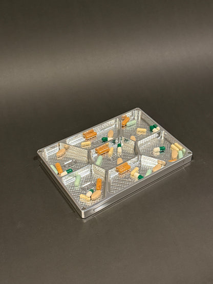 Raw machined Vitamin Vault Mega Lidless filled with tablets and capsules across seven labeled daily compartments.