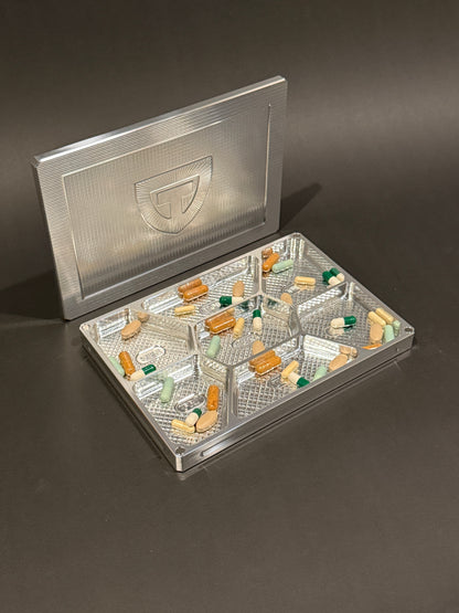 Raw machined Vitamin Vault Mega shown open with tablets and capsules in its seven labeled daily compartments.