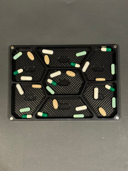 Top view of anodized black Vitamin Vault Mega Lidless filled across seven labeled daily compartments.