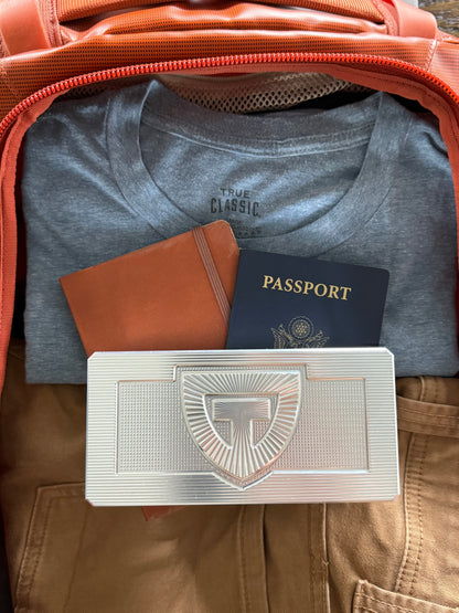 Closed TRT Vault Micro in Raw Machined packed in a carry-on beside a passport.