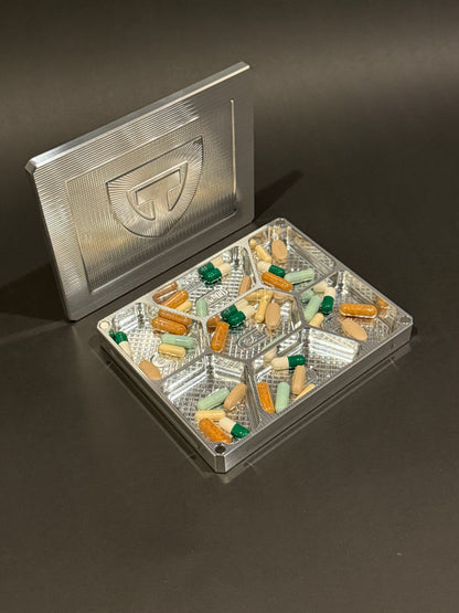 Open raw machined Vitamin Vault Mini filled with tablets and capsules, with its magnetic lid behind it.