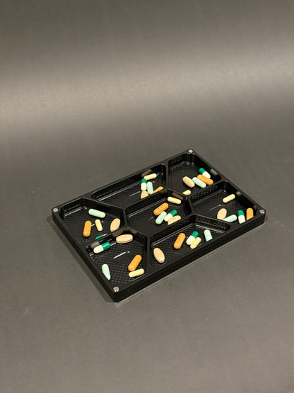 Anodized black Vitamin Vault Mega Lidless filled with tablets and capsules across seven labeled daily compartments.