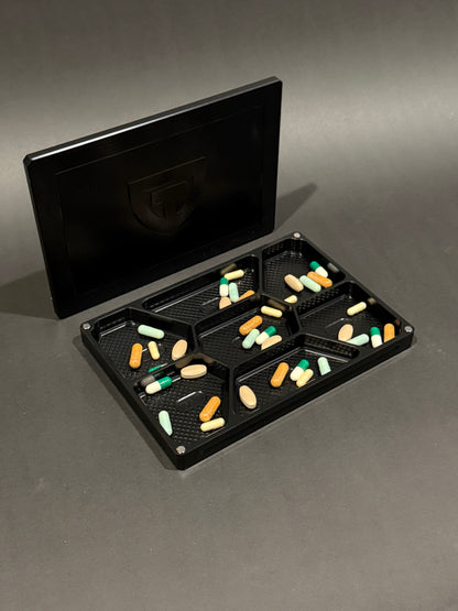 Anodized black Vitamin Vault Mega shown open with its magnetic lid, filled with tablets and capsules.
