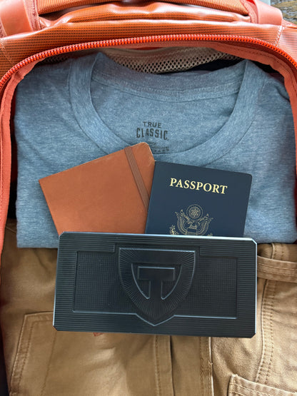 Closed TRT Vault Micro in Anodized Black packed in a carry-on beside a passport.