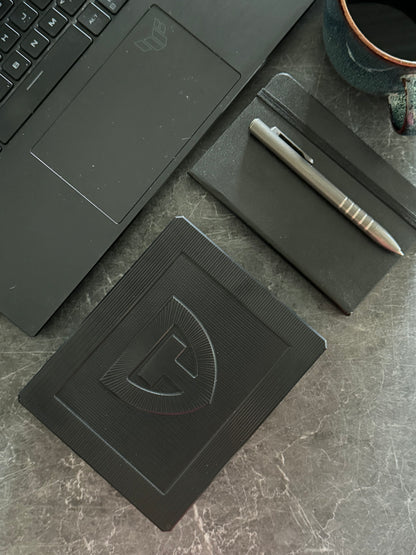 Closed TRT Vault Mini in Anodized Black on a desk with a laptop and notebook.