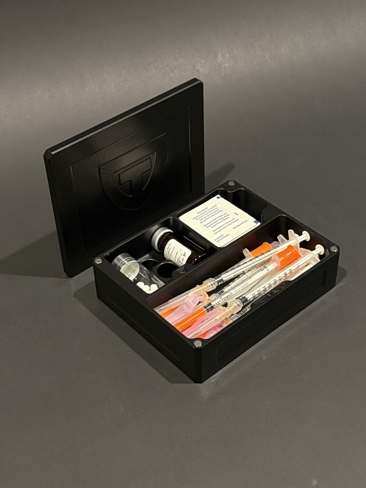 TRT Vault Mini in anodized black, shown open with vials, capped syringes and alcohol swabs. #black
