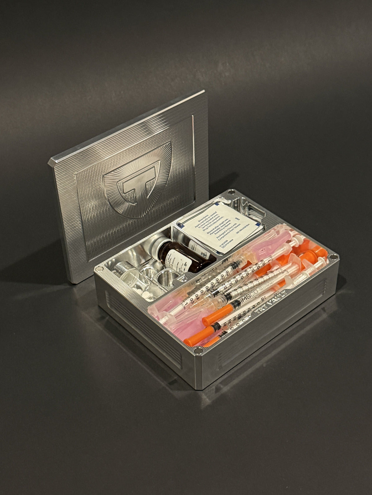 TRT Vault Mini in raw machined aluminum, shown open with a vial, capped syringes and alcohol swabs.