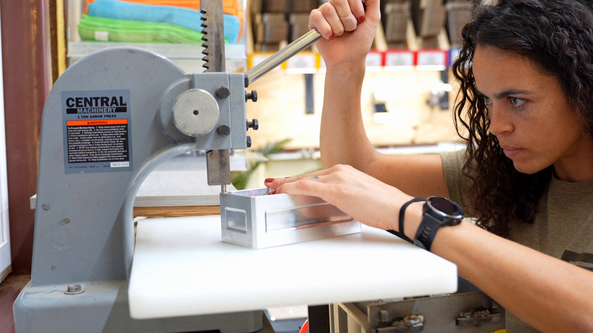 Hannah using a hand press to fit magnets into an aluminum Vault in the TRT Vault workshop.