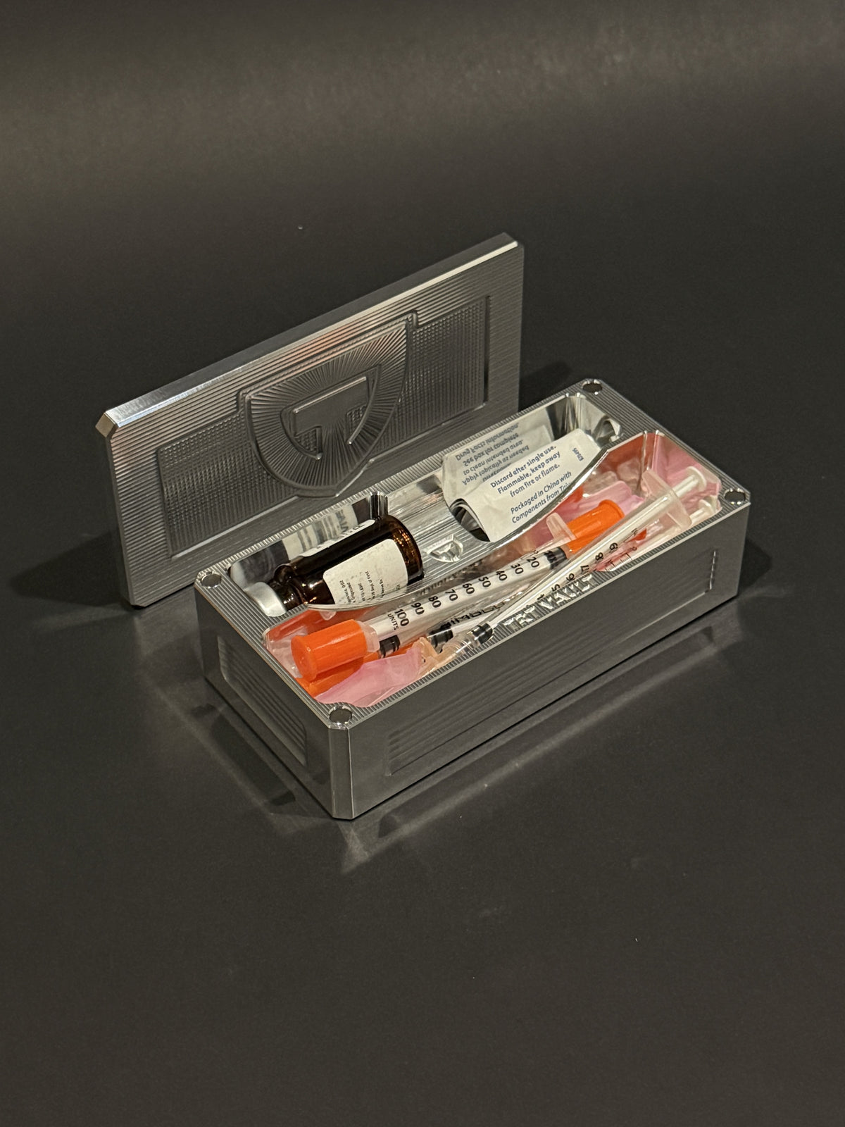 TRT Vault Micro in raw machined aluminum, shown open with a vial, capped syringes and alcohol swabs.