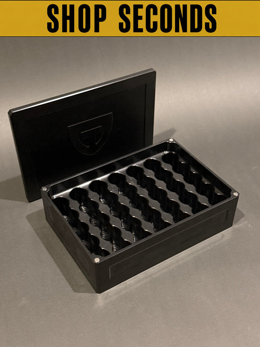 Shop Seconds black anodized Vial Vault Mega shown open and empty with magnetic lid, displaying upright vial storage slots.