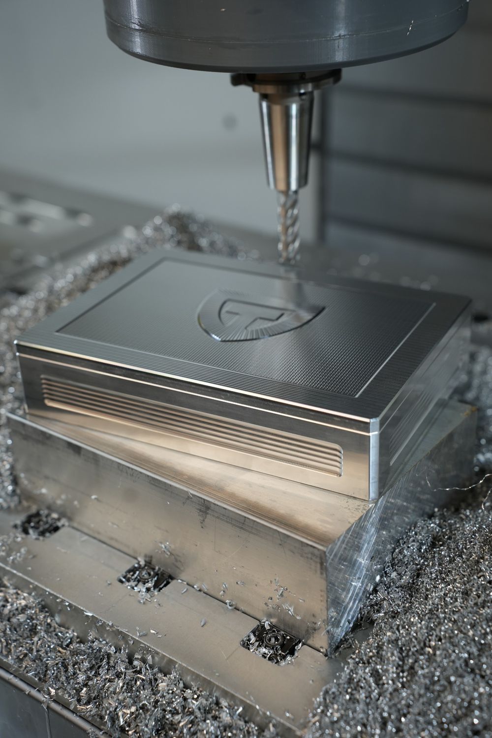 Closed raw aluminum TRT Vault beneath a CNC cutting tool, surrounded by metal shavings.