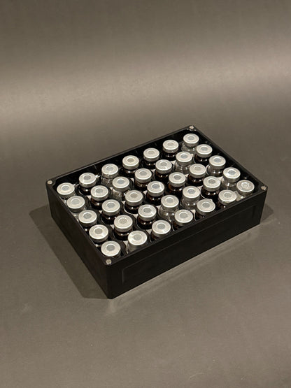 Lidless Vial Vault Mega in Anodized Black, filled with clear and amber glass vials standing upright.