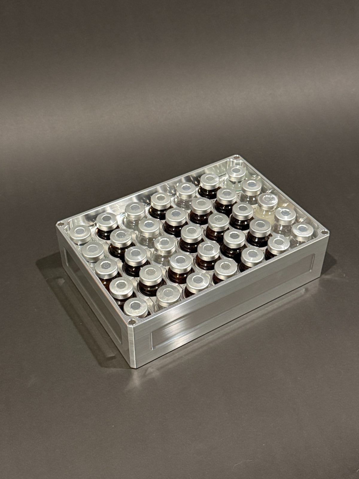Lidless Vial Vault Mega in Raw Machined, filled with clear and amber glass vials standing upright.