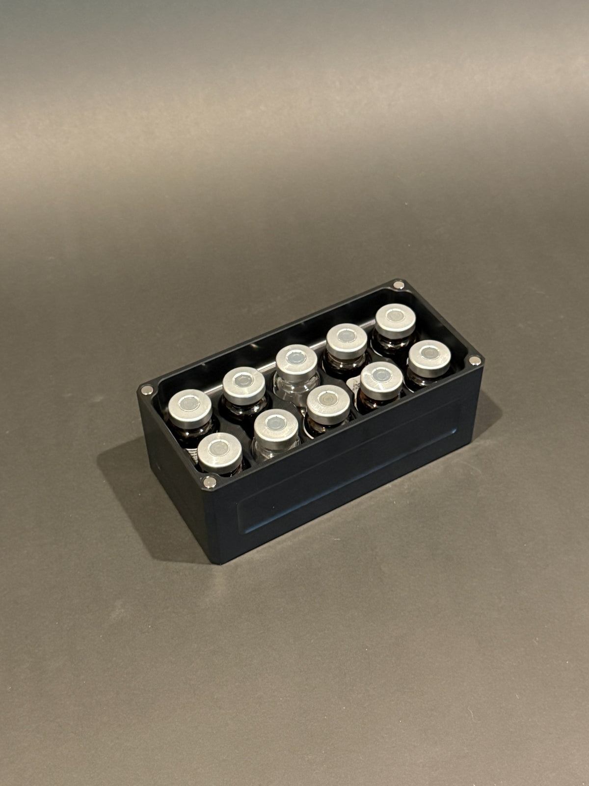 Lidless Vial Vault Micro in Anodized Black, filled with clear and amber glass vials standing upright.