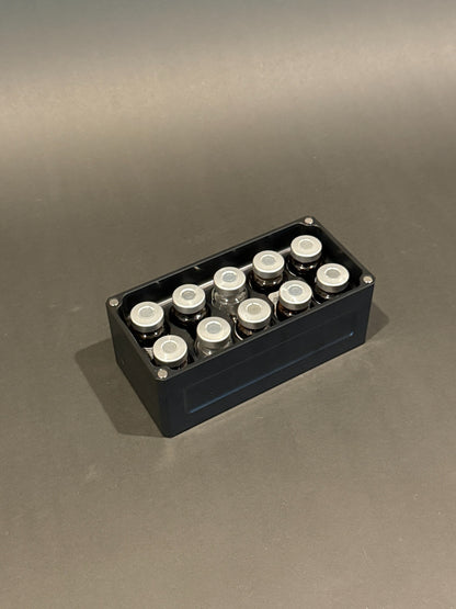Lidless Vial Vault Micro in Anodized Black, filled with clear and amber glass vials standing upright.