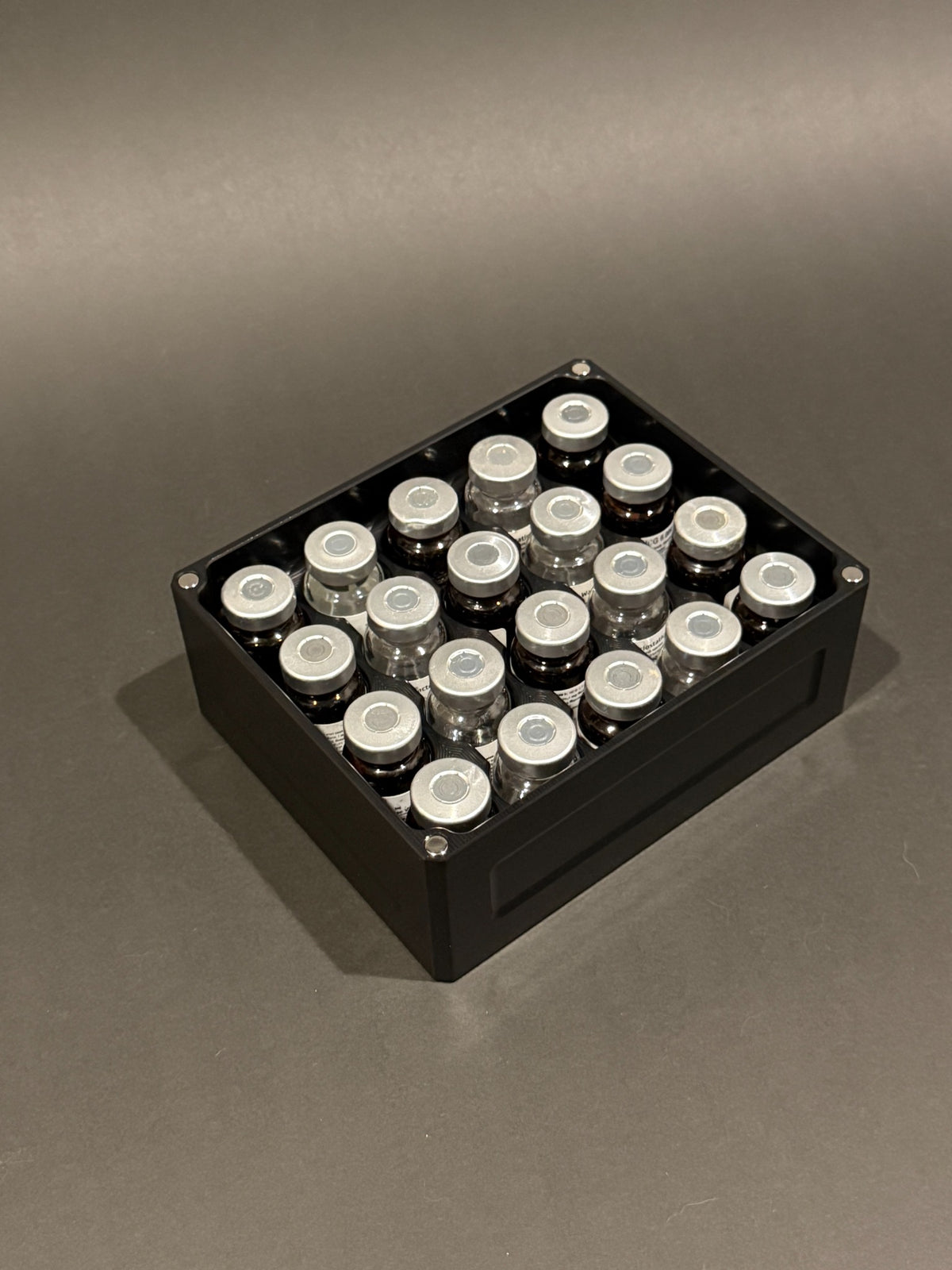 Lidless Vial Vault Mini in Anodized Black, filled with clear and amber glass vials standing upright.